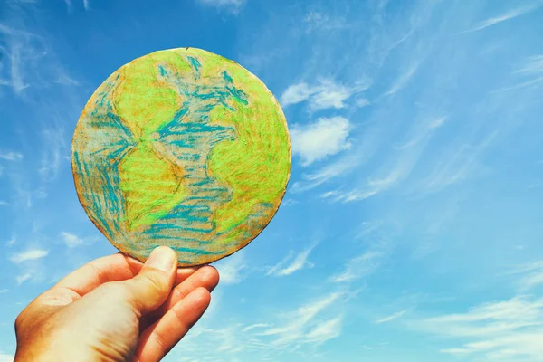 man hand holding earth globe in front of outdoor blue sky background