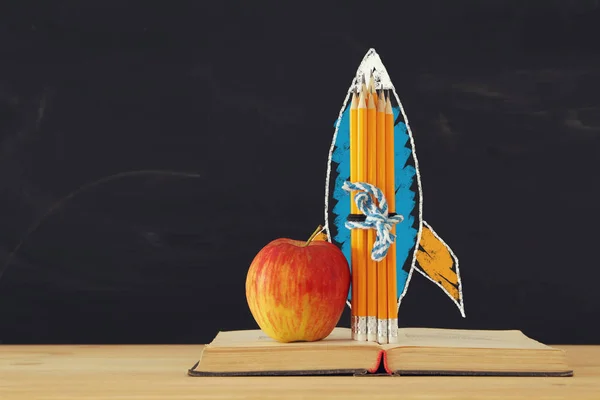学校のコンセプトです ロケットのスケッチと教室の黒板の前で開かれた本の鉛筆 — ストック写真