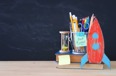 Geri okul kavramı. karton roket ve sınıf yazı tahtası önünde açık kitap üzerine kalem