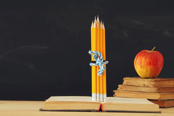back to school concept. stack of books and pencils over wooden desk in front of blackboard