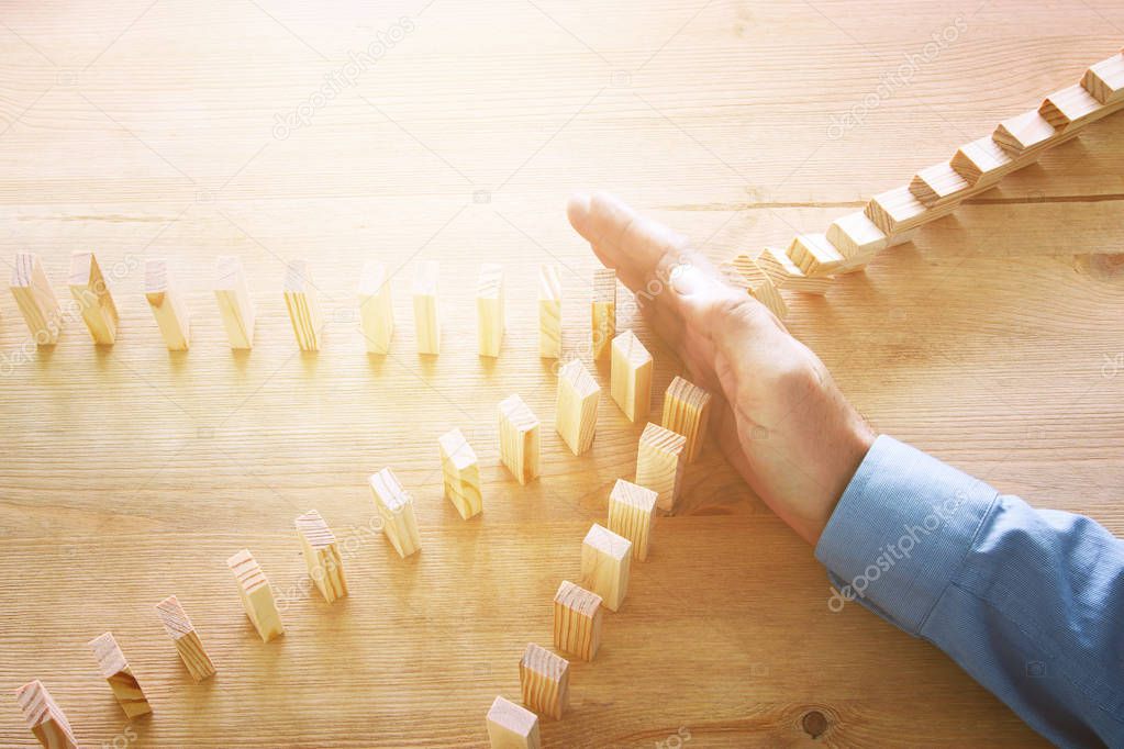 image of male hand stopping the domino effect. retro style image executive and risk control concept