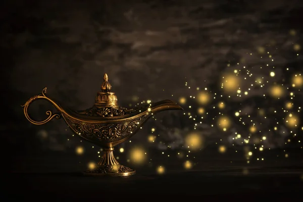 Image of magical mysterious aladdin lamp with glitter sparkle lights over black background. Lamp of wishes