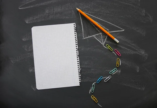 Top view image of plane sketch next to empty notebook paper over classroom blackboard background