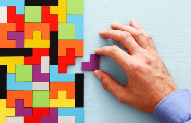 Bir adamın eli ahşap bir masanın üzerinde kare bir tangram yapbozu tutuyor.