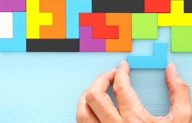 Bir adamın eli ahşap bir masanın üzerinde kare bir tangram yapbozu tutuyor.