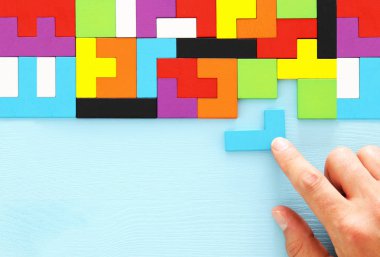 Bir adamın eli ahşap bir masanın üzerinde kare bir tangram yapbozu tutuyor.