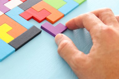 Bir adamın eli ahşap bir masanın üzerinde kare bir tangram yapbozu tutuyor.