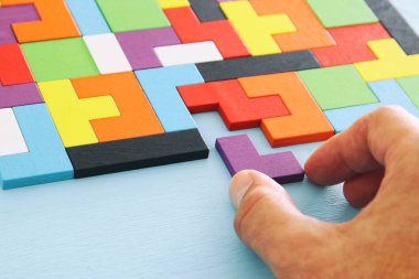 Bir adamın eli ahşap bir masanın üzerinde kare bir tangram yapbozu tutuyor.