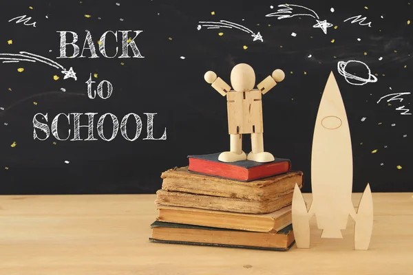 wooden rocket and space sketches with wooden dummy in front of classroom blackboard