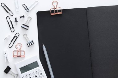 Hesap makinesi, siyah sayfaları ile açık not defteri ve diğer ofis malzemeleri ile beyaz ofis resepsiyon masası. Üstten görünüm