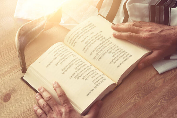 Jewish man hands holding a Prayer book, praying, next to tallit. Jewish traditional symbols. Rosh hashanah (jewish New Year holiday), Shabbat and Yom kippur concept