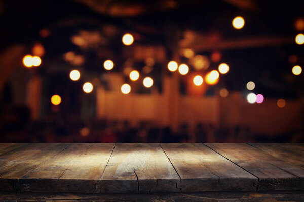 Image of wooden table in front of abstract blurred restaurant lights background