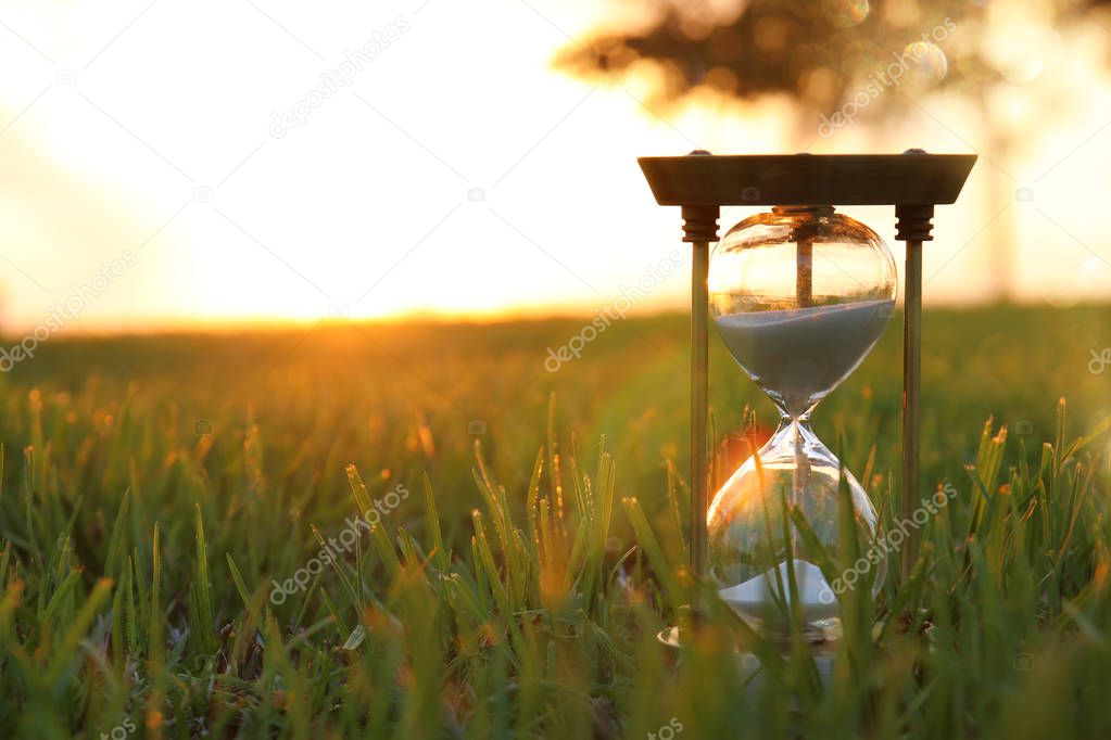 Hourglass in the grass time during sunset. vintage style