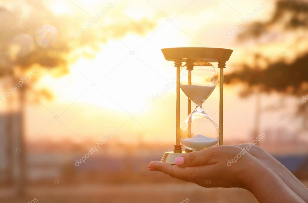 Young woman holding Hourglass during sunset. vintage style