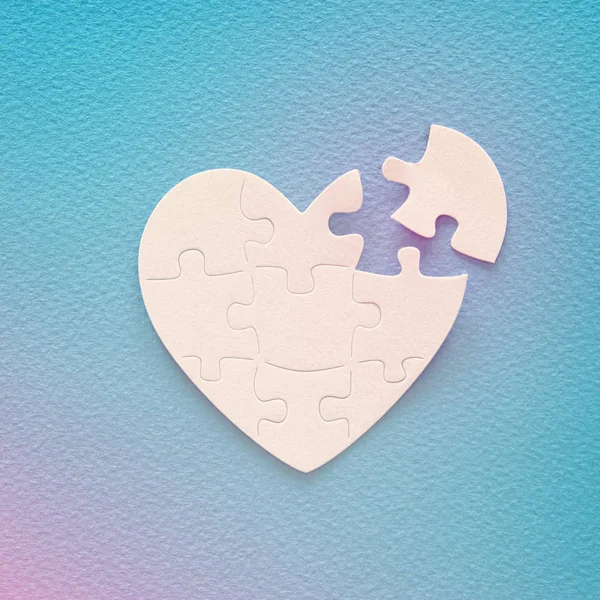 Top view image of paper white heart puzzle with missing piece over blue background. Health care, donate, world heart day and world health day concept