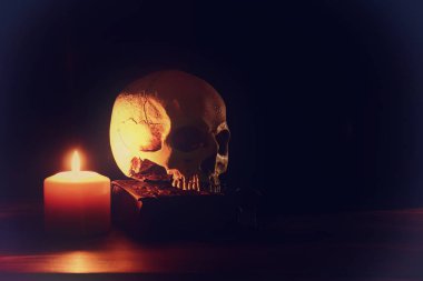 İnsan kafatası, eski kitap ve eski ahşap masa ve koyu arka plan üzerinde yanan mum