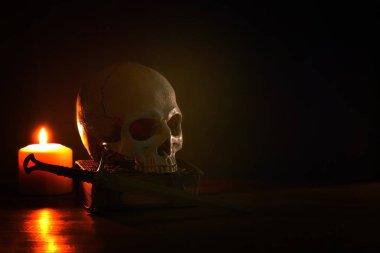 İnsan kafatası, eski kitap, kılıç ve eski ahşap masa ve koyu arka plan üzerinde yanan mum