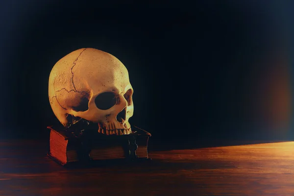 Human skull and old book over old wooden table and dark background