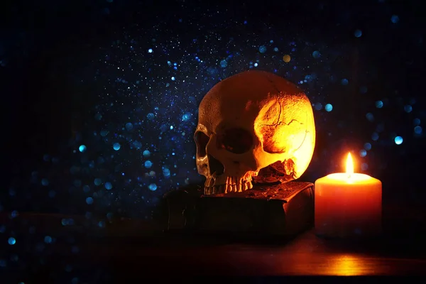 Human skull, old book and burning candle over old wooden table and darl background