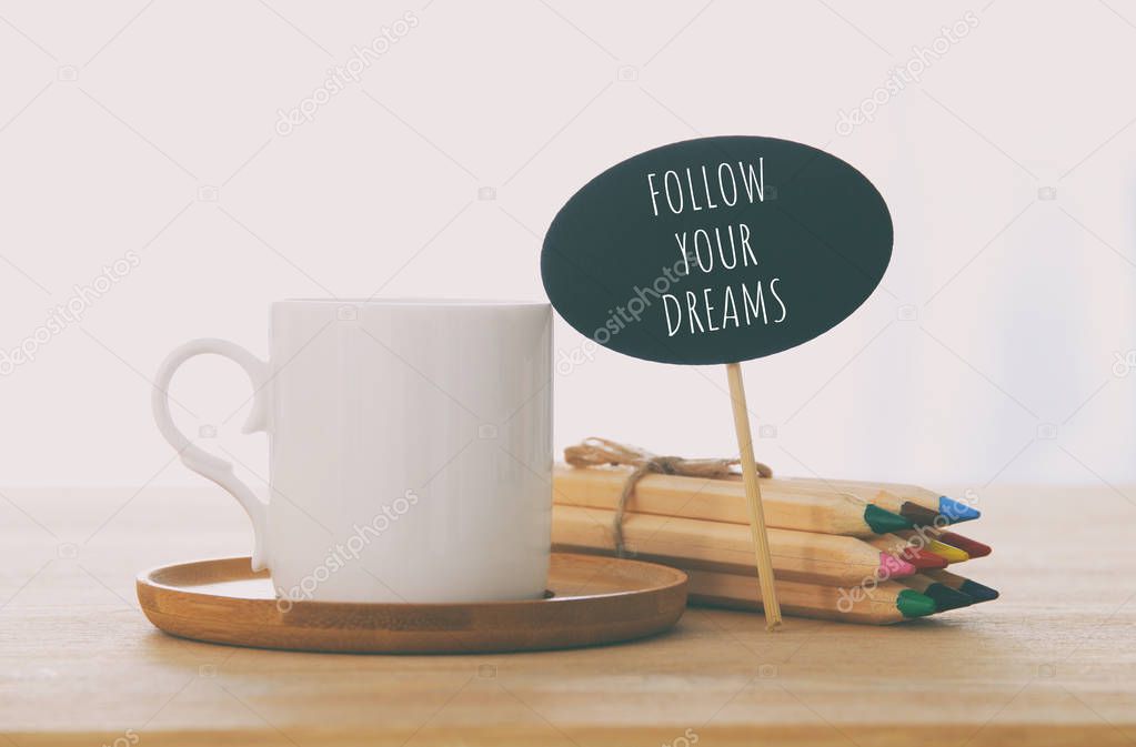 sign with text: FOLLOW YOUR DREAMS next to cup of coffee over wooden table