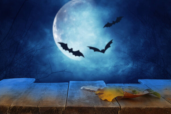 Halloween holiday concept. Empty rustic table in front of scary and misty night sky with black bats and full moon background. Ready for product display montage