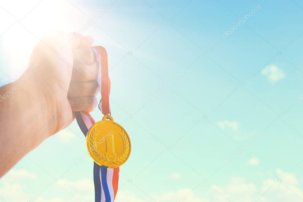 man hand raised, holding gold medal against sky. award and victory concept