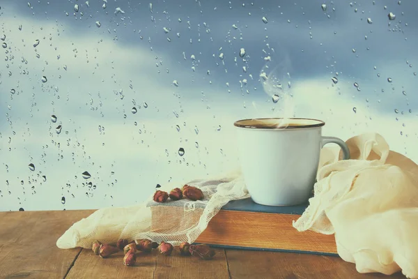 coffee cup on a rainy day over wooden table and window with rain drops background