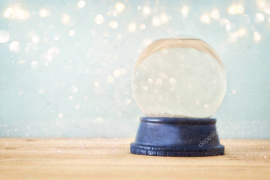 Empty Snow Globe over wooden table with glitter overlay. Magical Christmas concept. Copy space