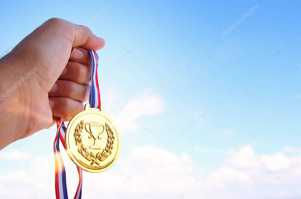 man hand raised, holding gold medal against sky. award and victory concept