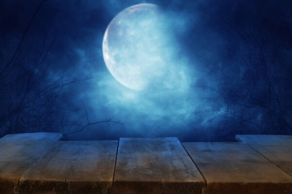 Halloween holiday concept. Empty rustic table in front of scary and misty night sky and full moon background. Ready for product display montage