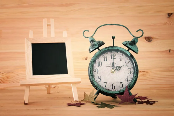 Image of autumn Time Change. Fall back concept. Dry leaves and vintage alarm Clock on rustic wooden table.