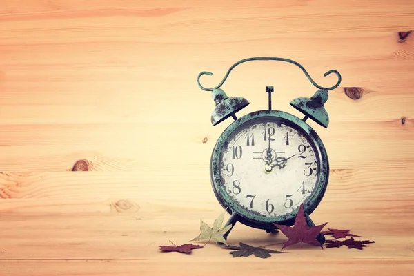 秋時間変更のイメージ。コンセプトにフォールバックします。乾燥した葉と素朴な木製のテーブルにビンテージの目覚まし時計. — ストック写真
