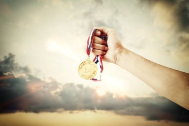 woman hand raised, holding gold medal against sky. award and victory concept clipart