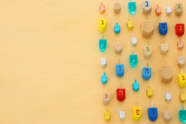 Image of jewish holiday Hanukkah with wooden dreidels colection (spinning top) over pastel yellow background