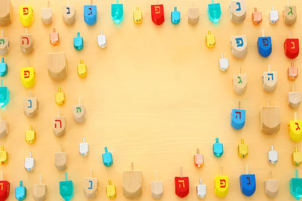 Image of jewish holiday Hanukkah with wooden dreidels colection (spinning top) over pastel yellow background