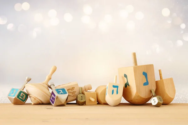 Nápis je židovský svátek Chanuka s dřevěnými dreidels (Káča) třpytky lesklé pozadí. — Stock fotografie
