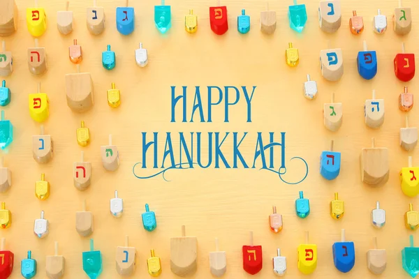 Image of jewish holiday Hanukkah with wooden dreidels colection (spinning top) over pastel yellow background