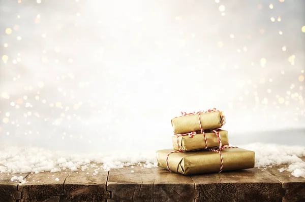 手工包裹的礼品盒的图像在木桌上覆盖着雪和银色闪闪发光的火箭条背景 — 图库照片