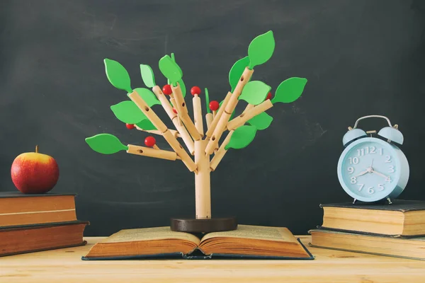 open book and wooden tree puzzle over blackboard background. education and knowledge concept