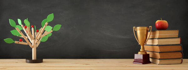 banner of open book, gold trophy and wooden tree puzzle over blackboard background. education and knowledge concept