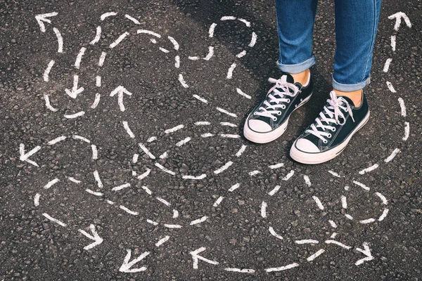 top view image of person in jeans and retro shoes standing over asphalt road with painted arrows showing different directions