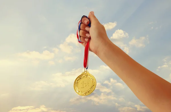 Mano de mujer levantada, sosteniendo la medalla de oro contra el cielo. premio y concepto de victoria. — Foto de Stock