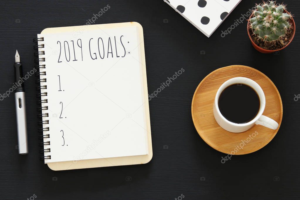 Top view 2019 goals list with notebook, cup of coffee over wooden black desk