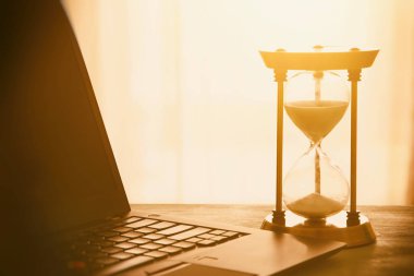 Laptop üzerinde ahşap masa başında ofis, işyeri veya ev ve kum saati görüntüsü. Filtre vintage