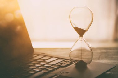 Laptop üzerinde ahşap masa başında ofis, işyeri veya ev ve kum saati görüntüsü. Filtre vintage