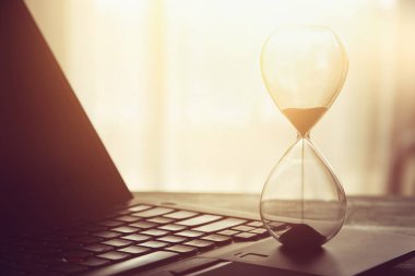 Laptop üzerinde ahşap masa başında ofis, işyeri veya ev ve kum saati görüntüsü. Filtre vintage