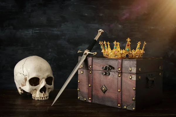 low key image of beautiful queen/king crown over old chest , human skull and sword. fantasy medieval period
