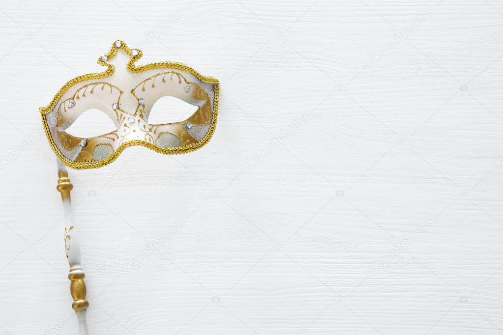carnival party celebration concept with elegant gold mask on stick over white wooden background. Top view