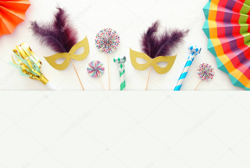 carnival party celebration concept with gold and silver masks over white wooden background and colorful fans. Top view