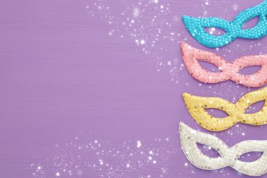 Karnaval parti kutlama kavramı ile mor ahşap arka plan üzerinde renkli pastel pembe, altın, gümüş ve mavi maske. Üstten görünüm